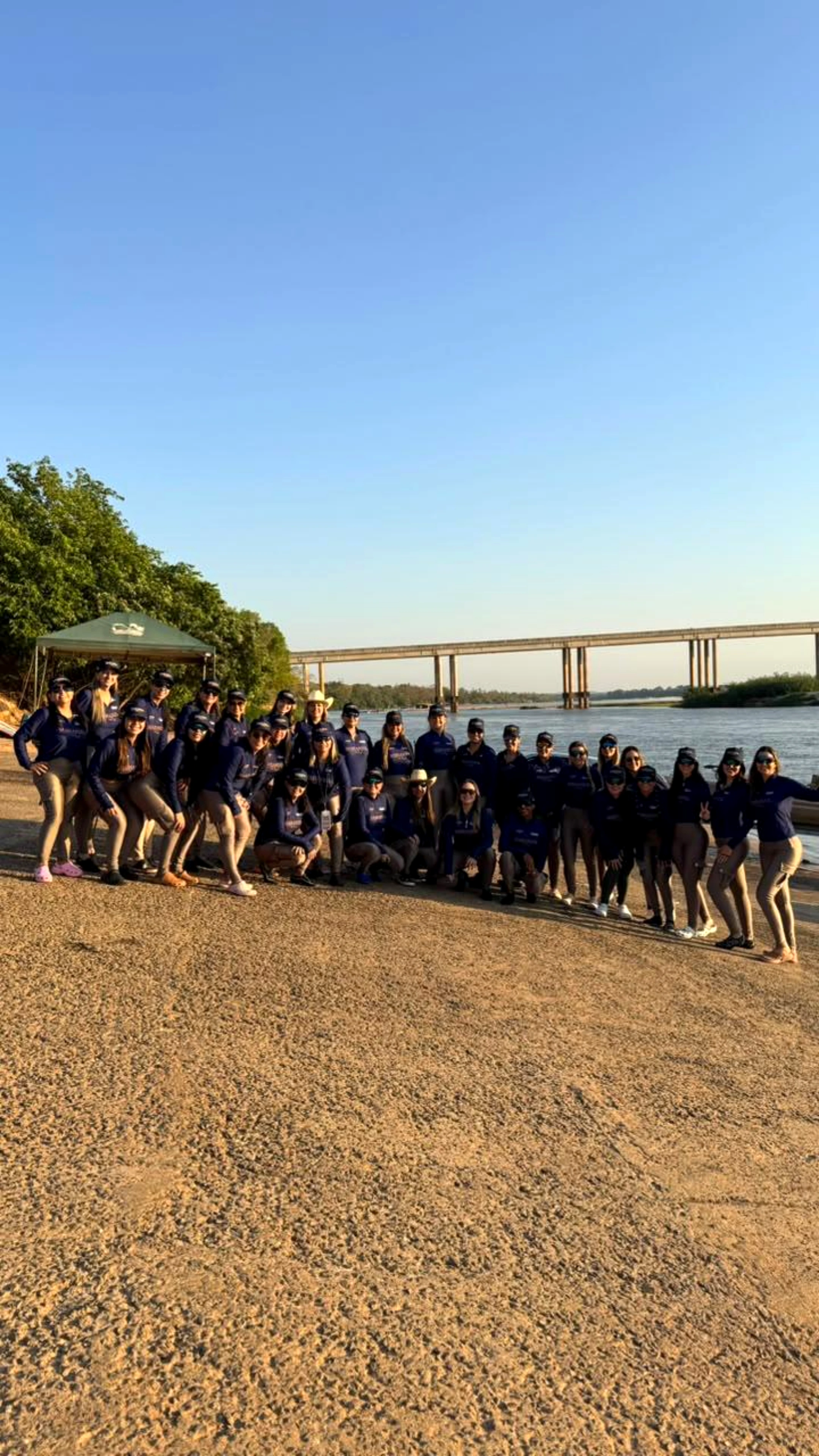 Grupo de mulheres da Marianzol reunido à beira do rio com uma ponte ao fundo