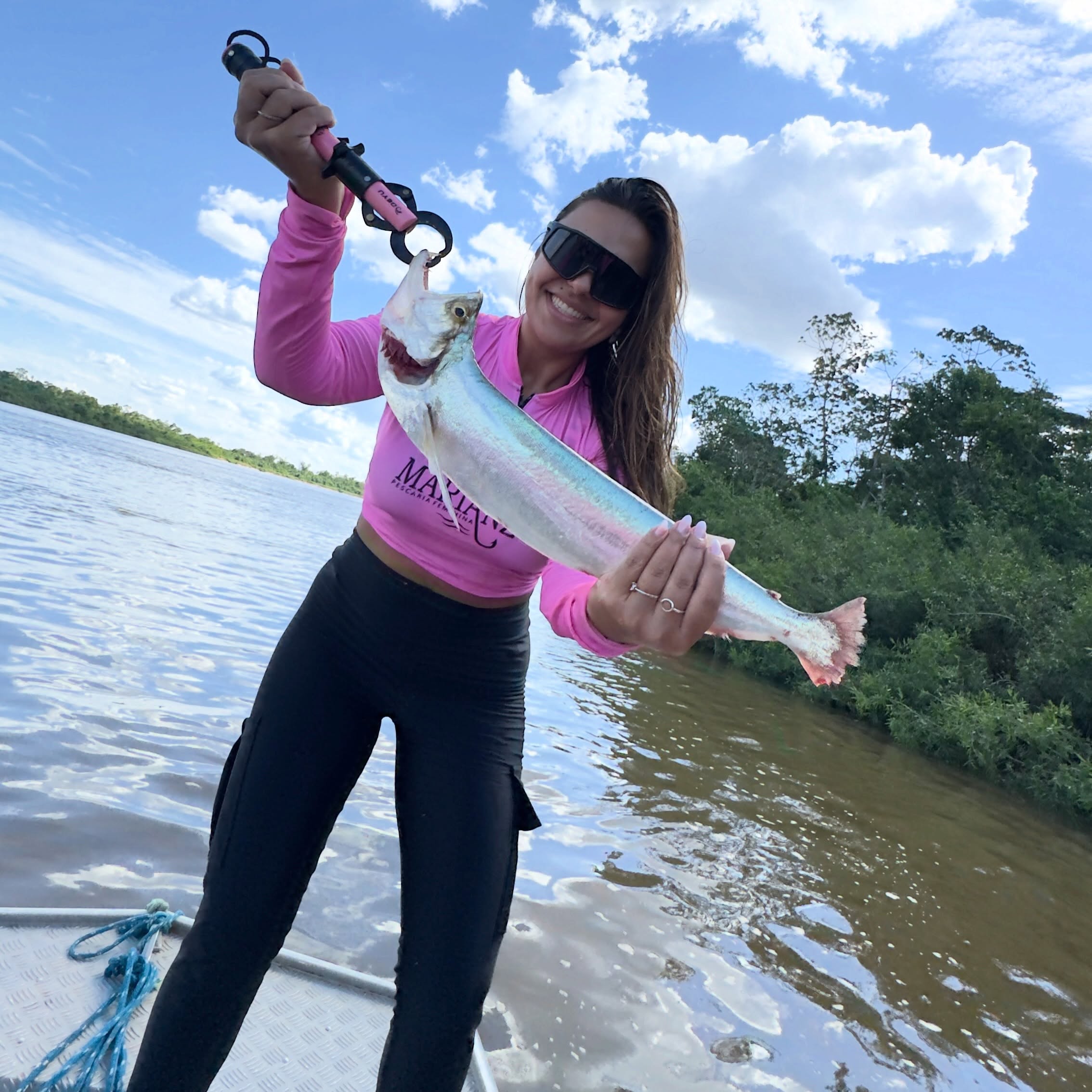 Pescadora de camiseta rosa com peixe na margem do rio